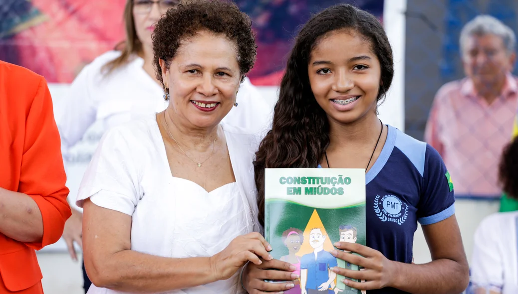 Regina Sousa entrega livro para aluna