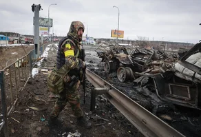 Homem armado fica ao lado dos restos de um veículo militar russo em Bucha