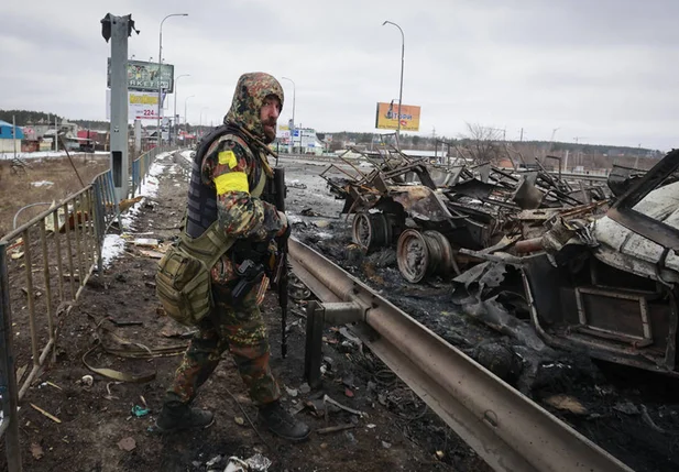 Homem armado fica ao lado dos restos de um veículo militar russo em Bucha
