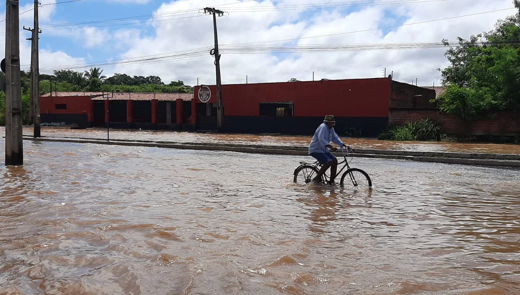 Senhor passa de bicicleta por trecho alagado