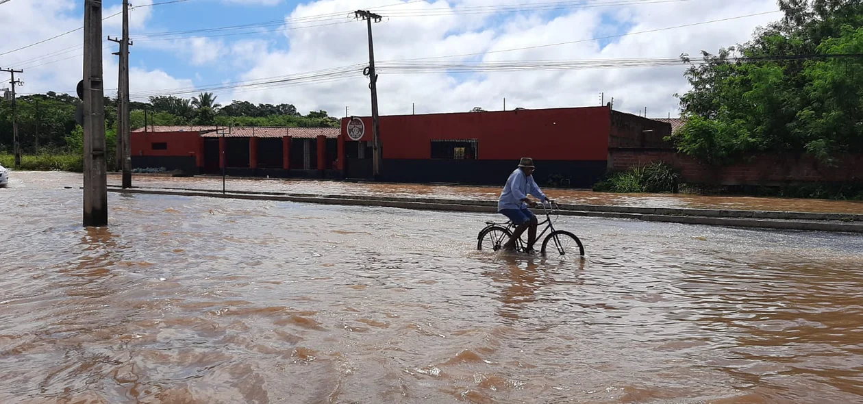 Senhor passa de bicicleta por trecho alagado