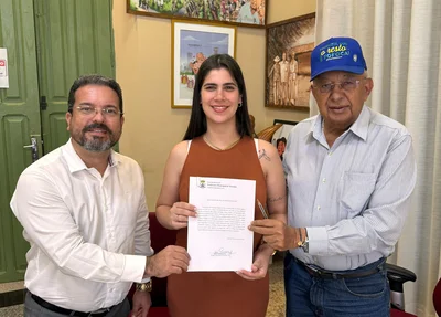 Vereadora Thanandra Sarapatinhas ao lado do prefeito Dr. Pessoa (à dir.) e do secretário de Governo, Michel Saldanha (à esq.) com o documento de cessão do terreno