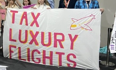 Cartaz com a frase “Tax luxury flights” (“Taxe voos de luxo”).