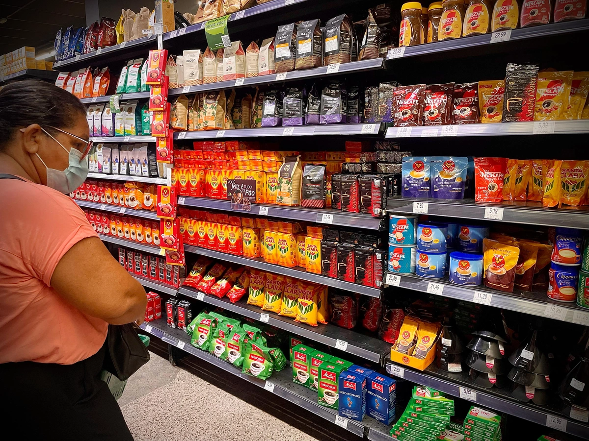 Mulher verificando o preço do café nas prateleiras do supermercado