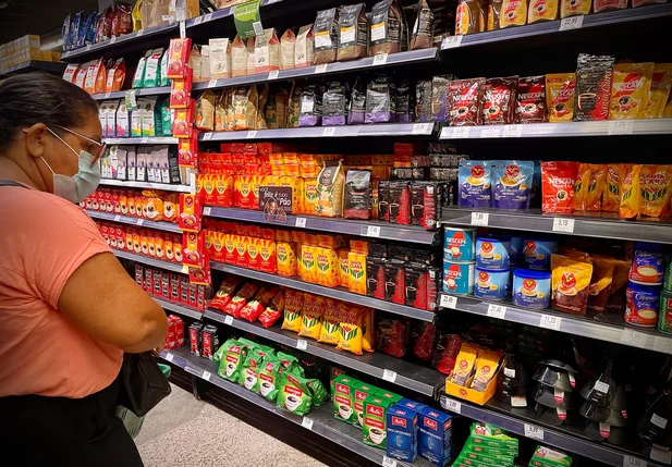 Mulher verificando o preço do café nas prateleiras do supermercado