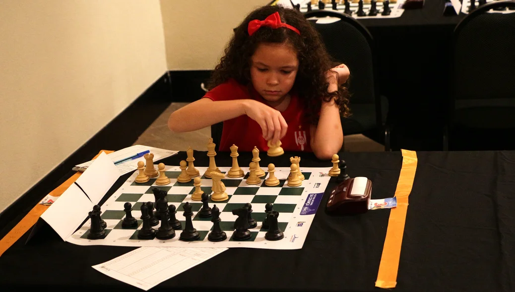 Menina mexendo peça de xadrez no Festival Nacional da Criança (FENAC)
