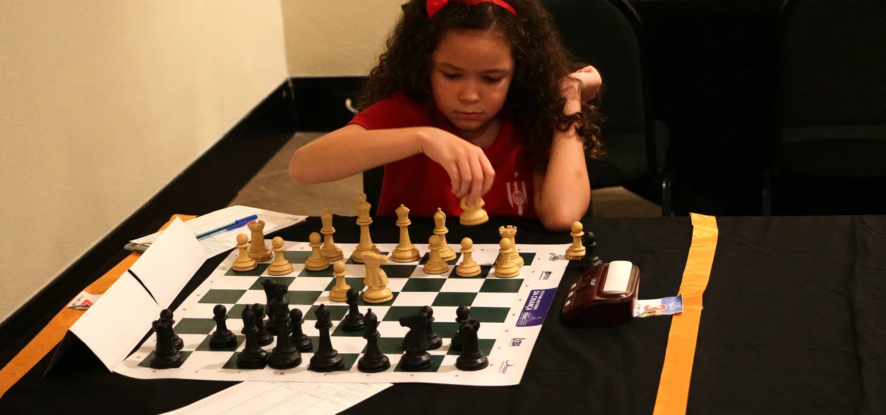 Menina mexendo peça de xadrez no Festival Nacional da Criança (FENAC)