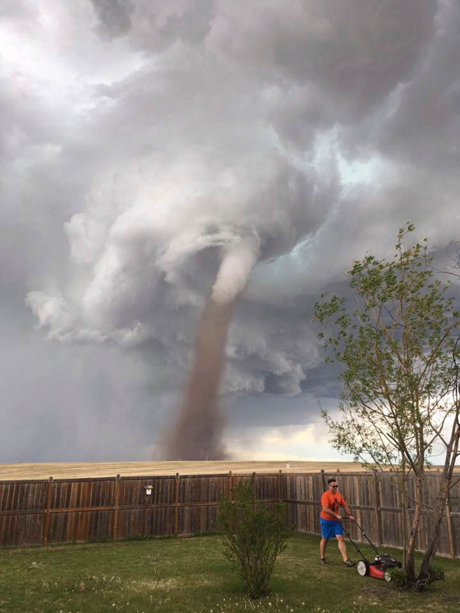 Homem corta grama enquanto tornado se aproxima