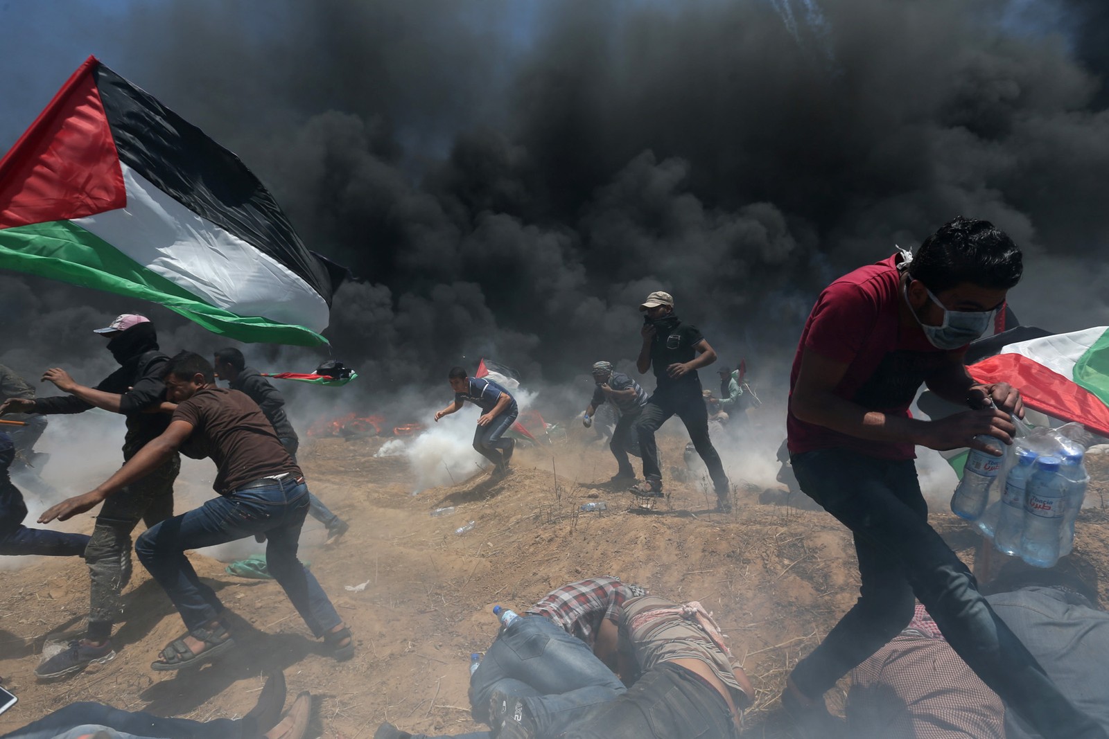 Manifestantes palestinos correm para se proteger de tiros e bombas de gás atiradas por tropas israelenses durante protesto na fronteira entre Israel e Gaza contra a inauguração de embaixada dos EUA