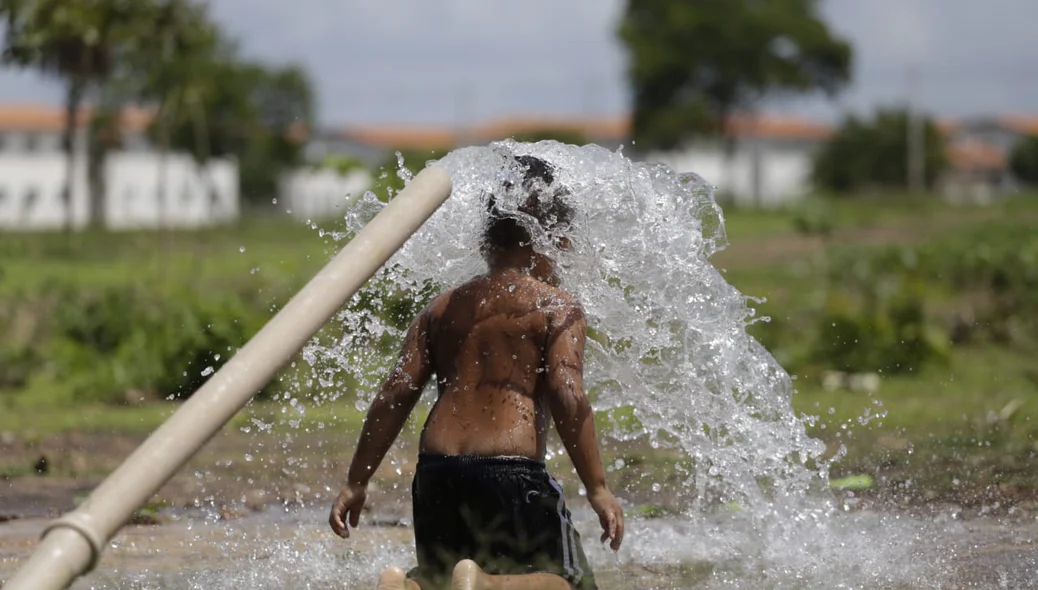 Criança tomando banho em cano que estourou 