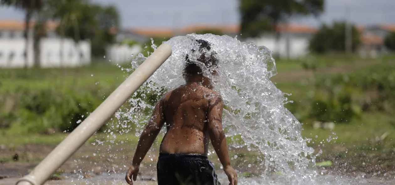 Criança tomando banho em cano que estourou 