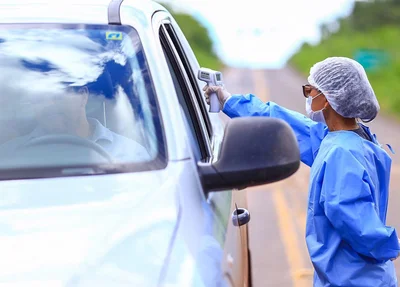 Agente de saúde mede temperatura de passageiros de veículo